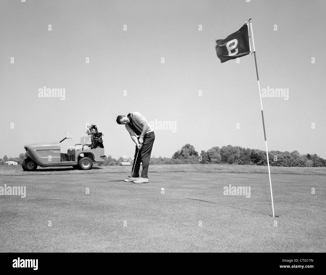 Anni sessanta uomo giocando a golf putting pallina da golf verso la bandiera e la tazza di foro sul 9TH VERDE PRIMAVERA ESTATE ALL'APERTO Foto Stock
