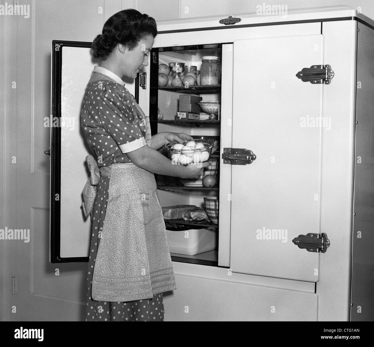 1930s massaia in grembiule PRENDENDO LE UOVA AL DI FUORI DEL RECIPIENTE dal congelatore Foto Stock