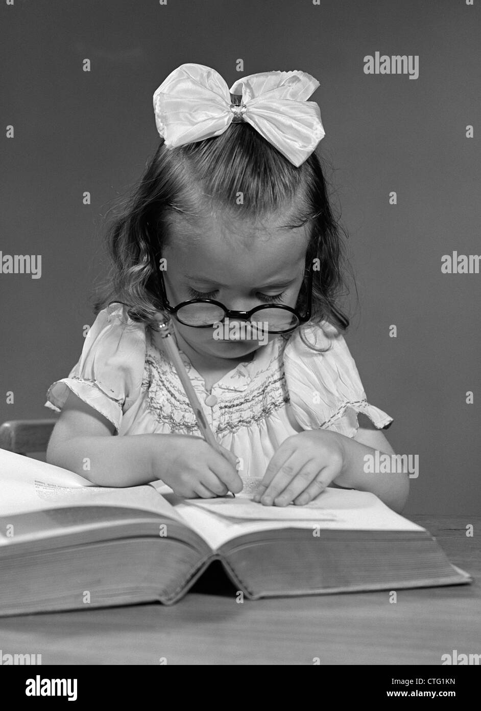 1940s ragazza con grandi bicchieri arrotondati e un grande nastro bianco BOW nei capelli copia da un libro con una matita Foto Stock