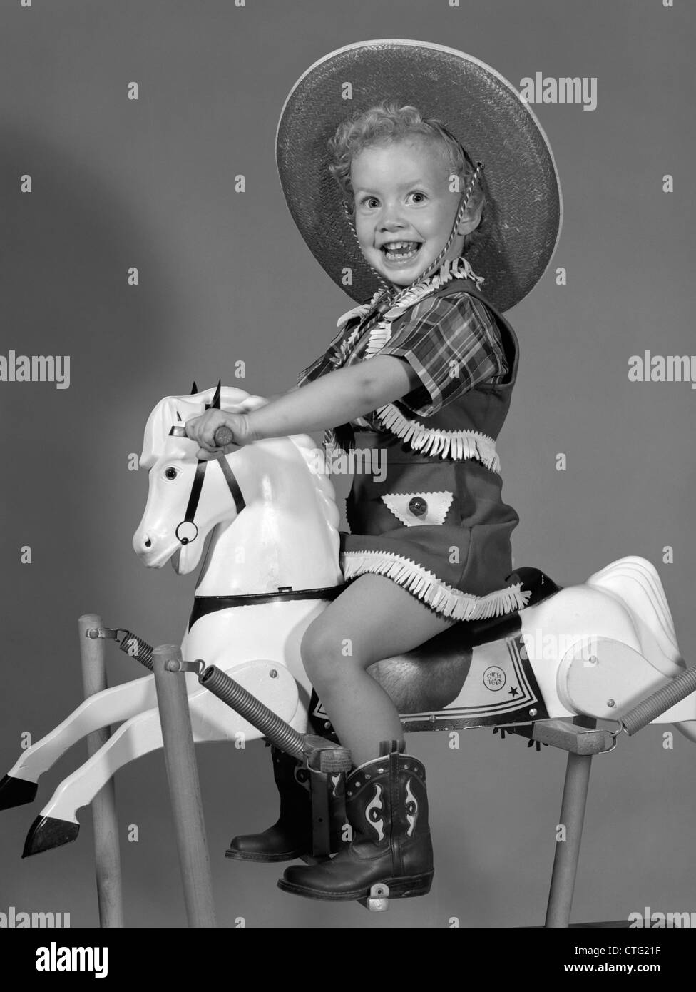 Anni Cinquanta ragazza vestita come COWGIRL riding del cavallo a dondolo Foto Stock