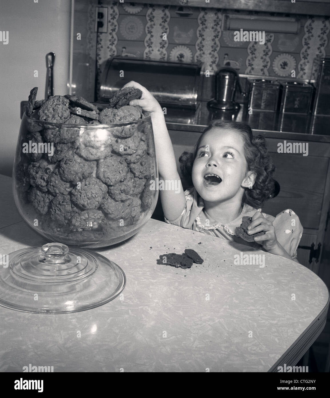 Anni Cinquanta WIDE-EYED ragazza con bocca agape che arrivano fino in cookie JAR prendendo un altro con pezzetti di cioccolato Foto Stock