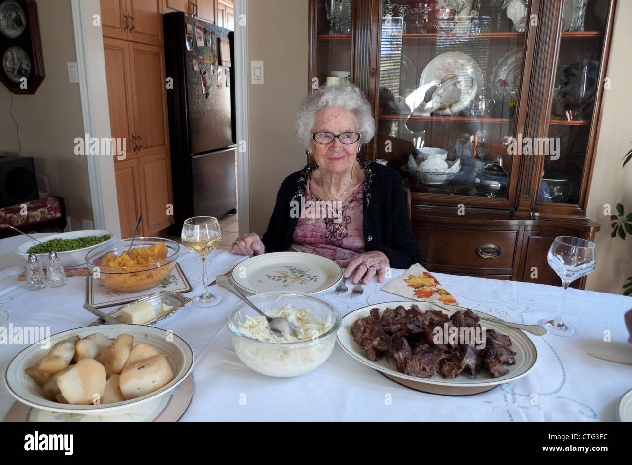 Un anziano sorridente donna senior seduti ad un tavolo da pranzo in attesa per i membri della famiglia ad unirsi a lei in Ontario Canada KATHY DEWITT Foto Stock