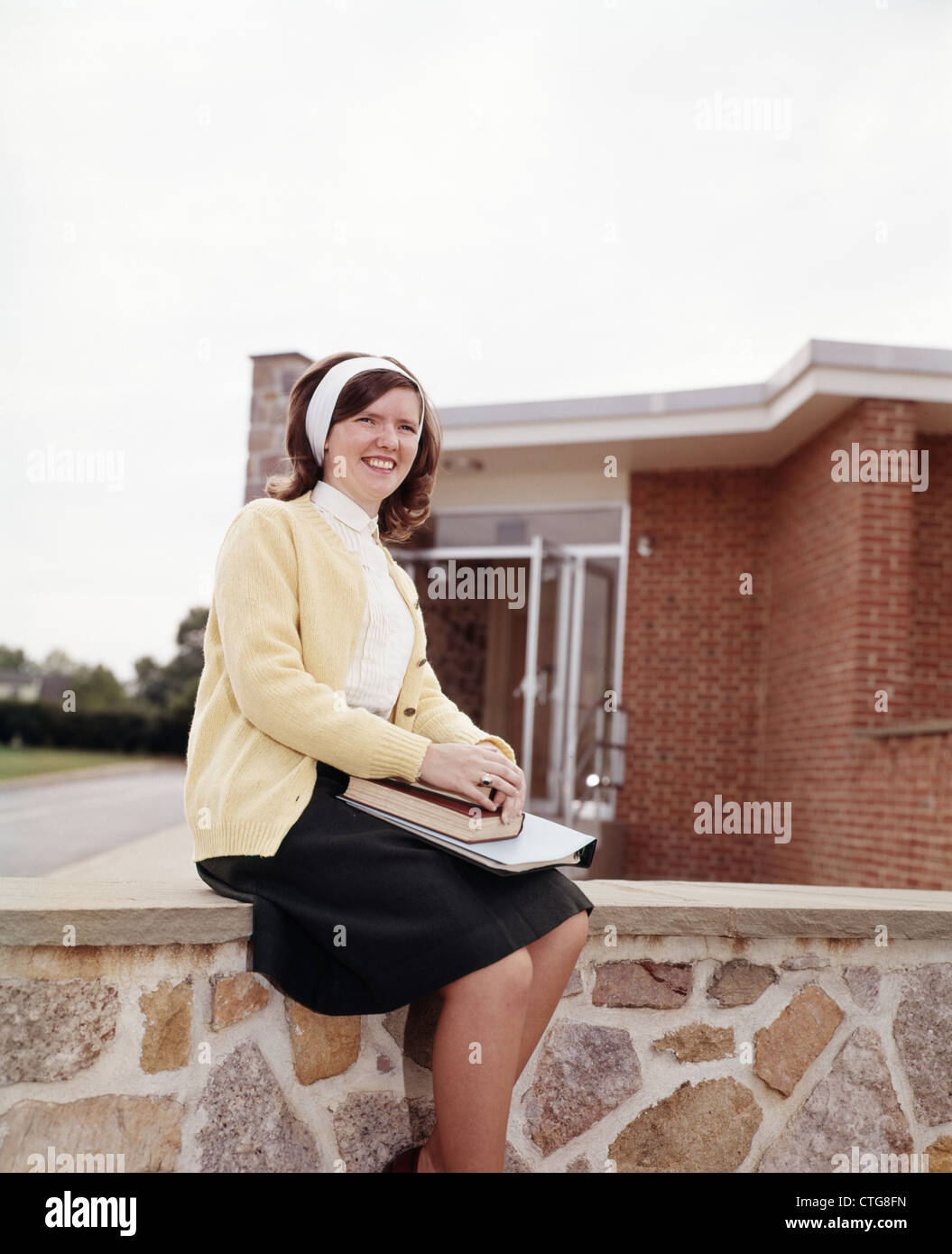 1960 anni sessanta sorridente ragazza TEEN MAGLIONE & gonna sedersi sui gradini di pietra edificio in mattoni Foto Stock