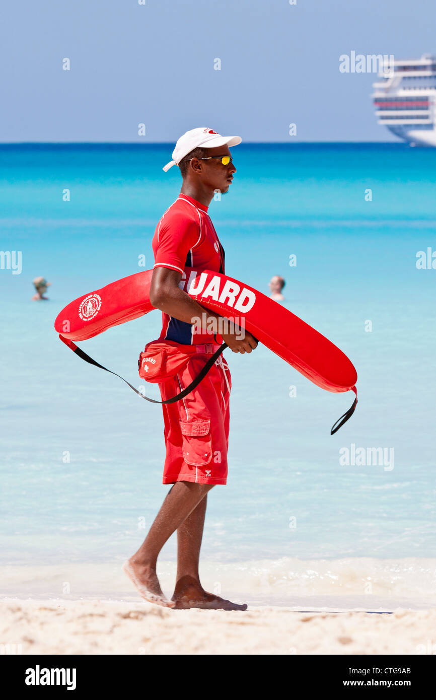 Giovane maschio nero lifeguard passeggiate sulla spiaggia con il salvataggio del dispositivo a galleggiante a Half Moon Cay, Bahamas Foto Stock