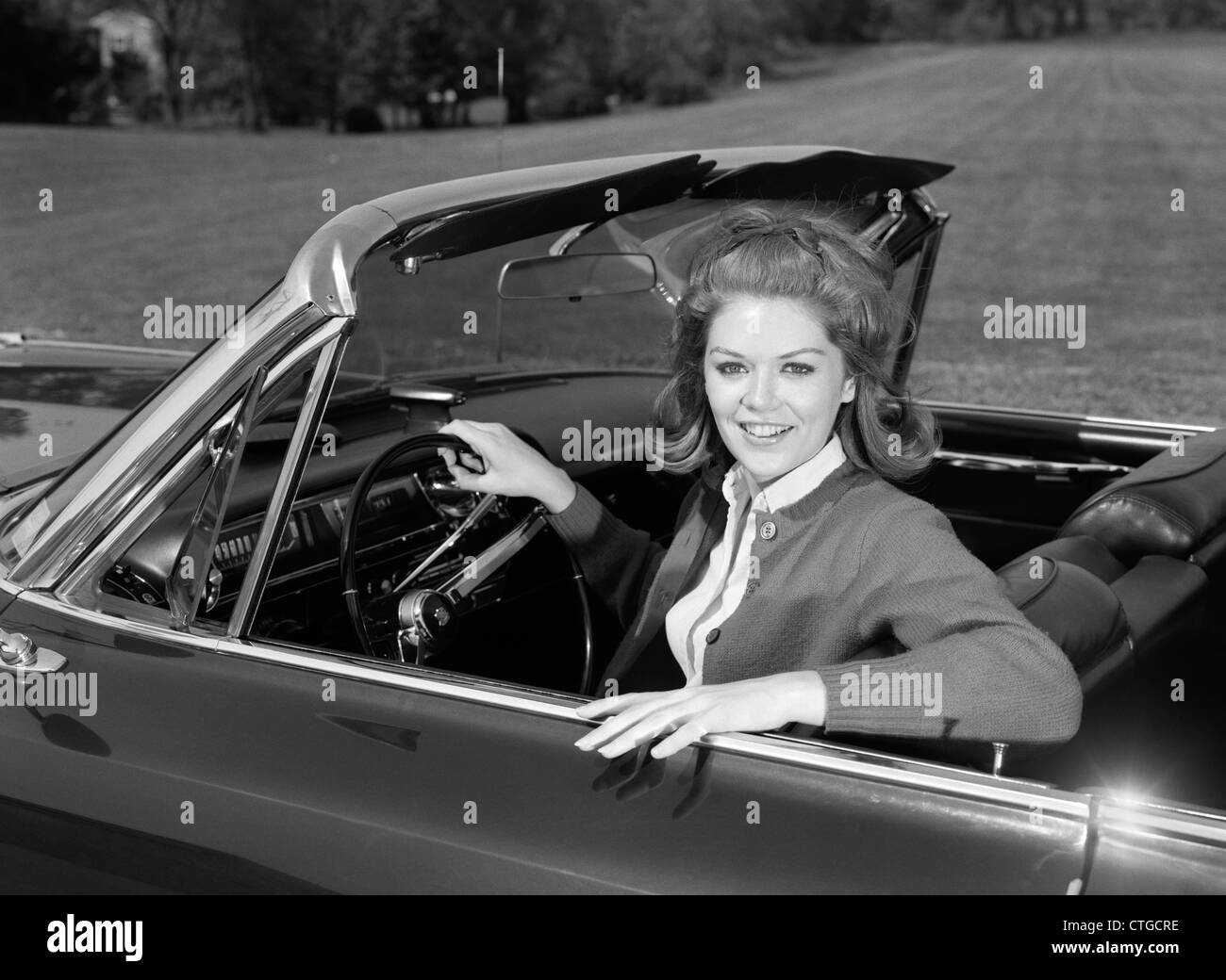 Anni sessanta sorridente TEENAGE donna seduta in autovettura convertibile guardando la fotocamera Foto Stock