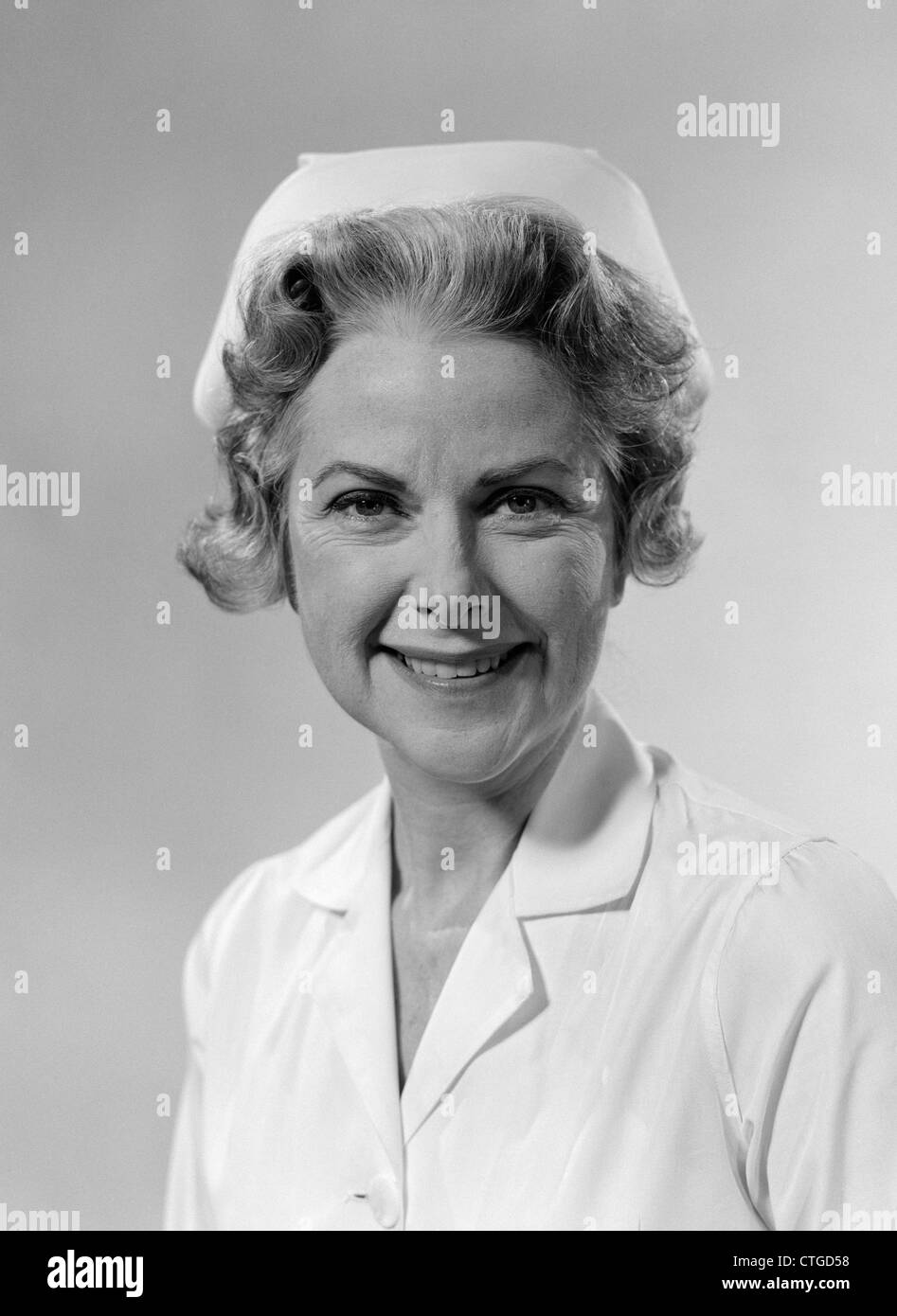 Anni sessanta ritratto di donna sorridente infermiere indossando il cappuccio BIANCO E UNIFORME DI STUDIO INDOOR Foto Stock