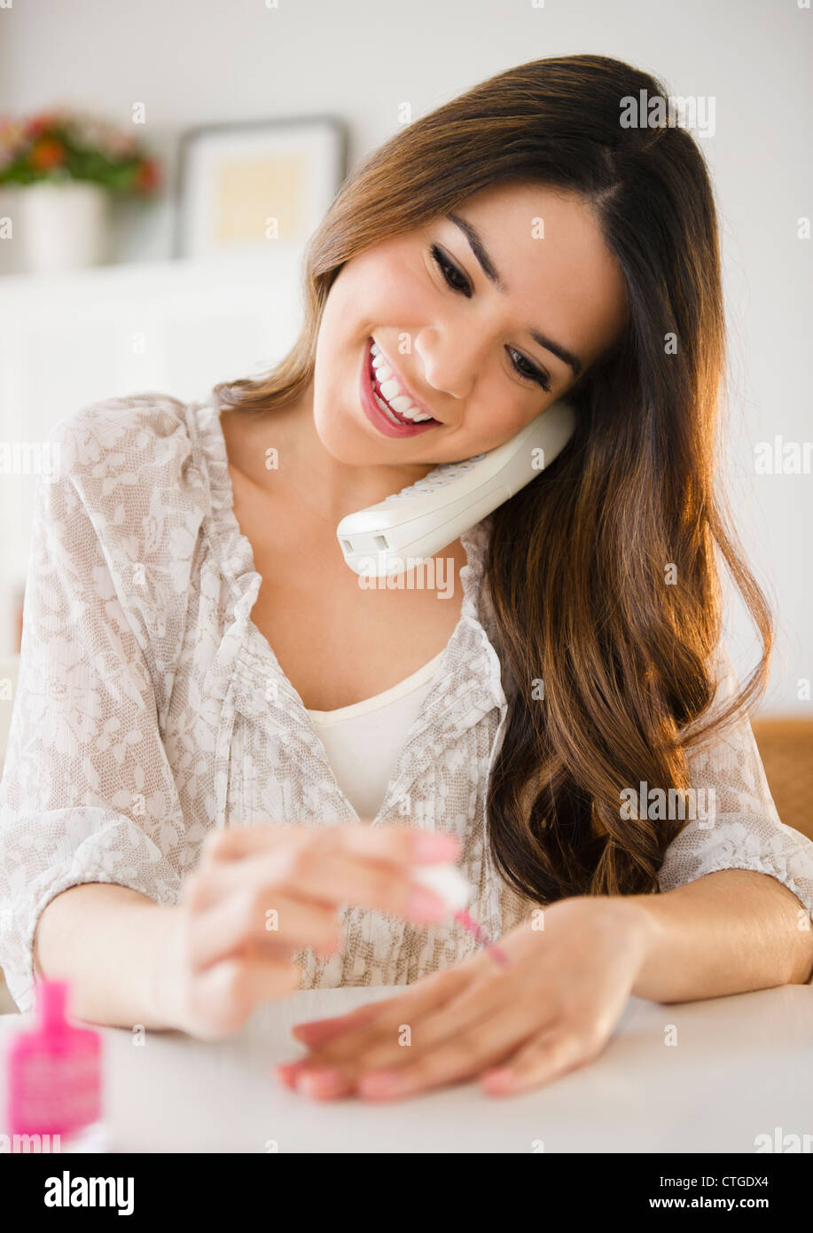 Donna ispanica parlando al telefono e pittura le unghie Foto Stock