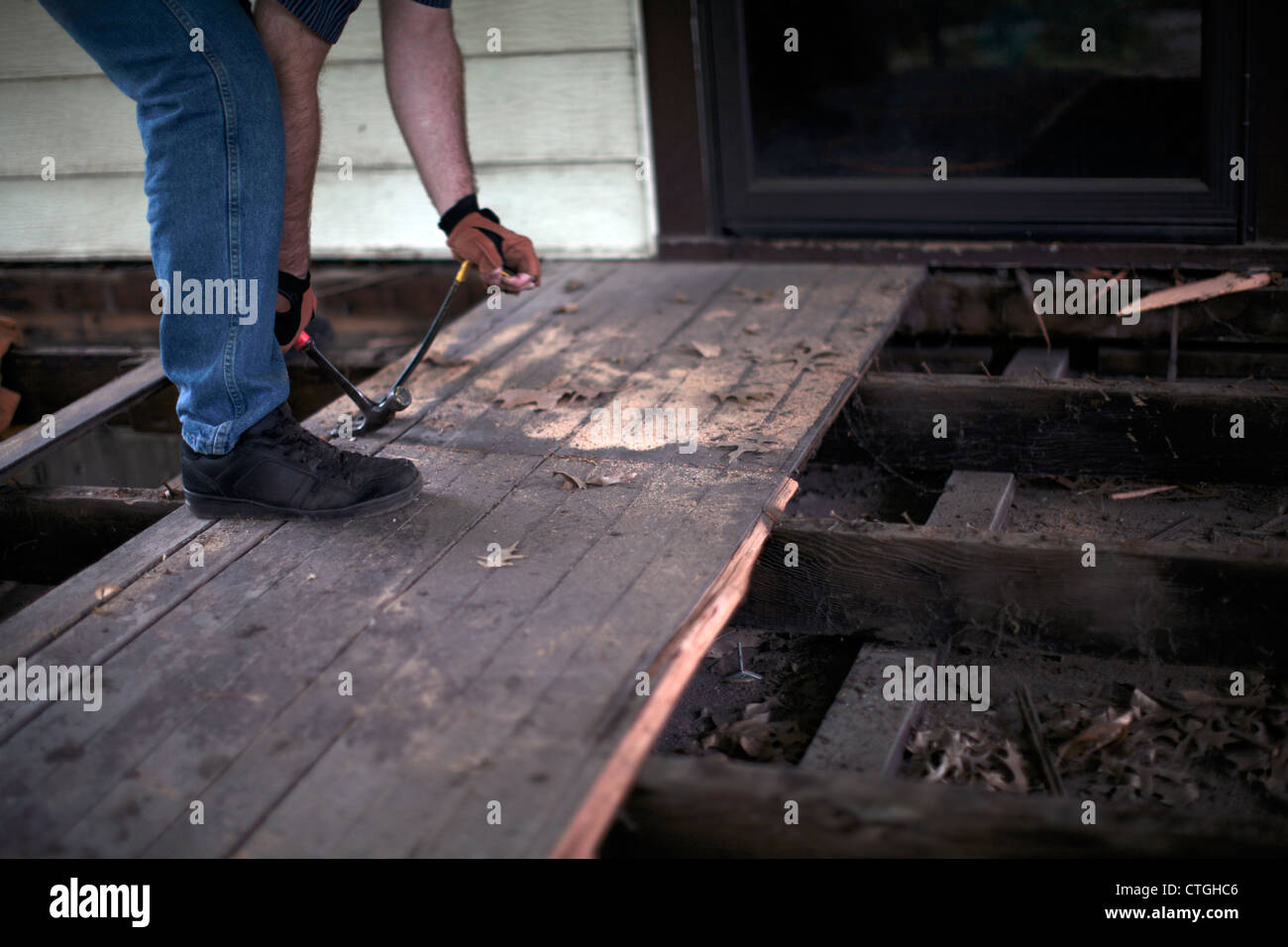 Uomo che utilizza un martello e una leva per rimuovere il portico decking listoni. Foto Stock