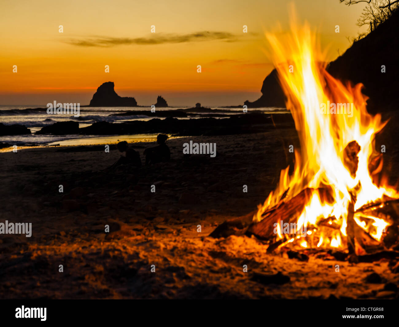 Un falò scintillante sorge in alto sulla spiaggia al tramonto Foto Stock