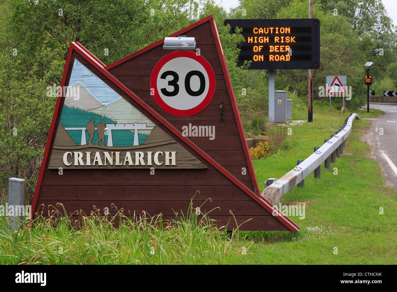 Il nome del luogo e 30 mph segnale di limite di velocità sulla A85 con la matrice di segno 'avvertenza prestare attenzione ad alto rischio di cervidi' Crianlarich Scozia UK Foto Stock