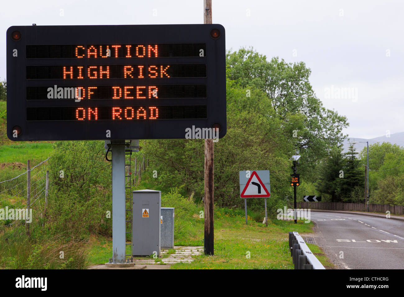 Segno di matrice su un85 avvertimento "fare attenzione ad alto rischio di cervo sulla strada' con lenta prima di piegare e High Fence Crianlarich Scozia UK Foto Stock