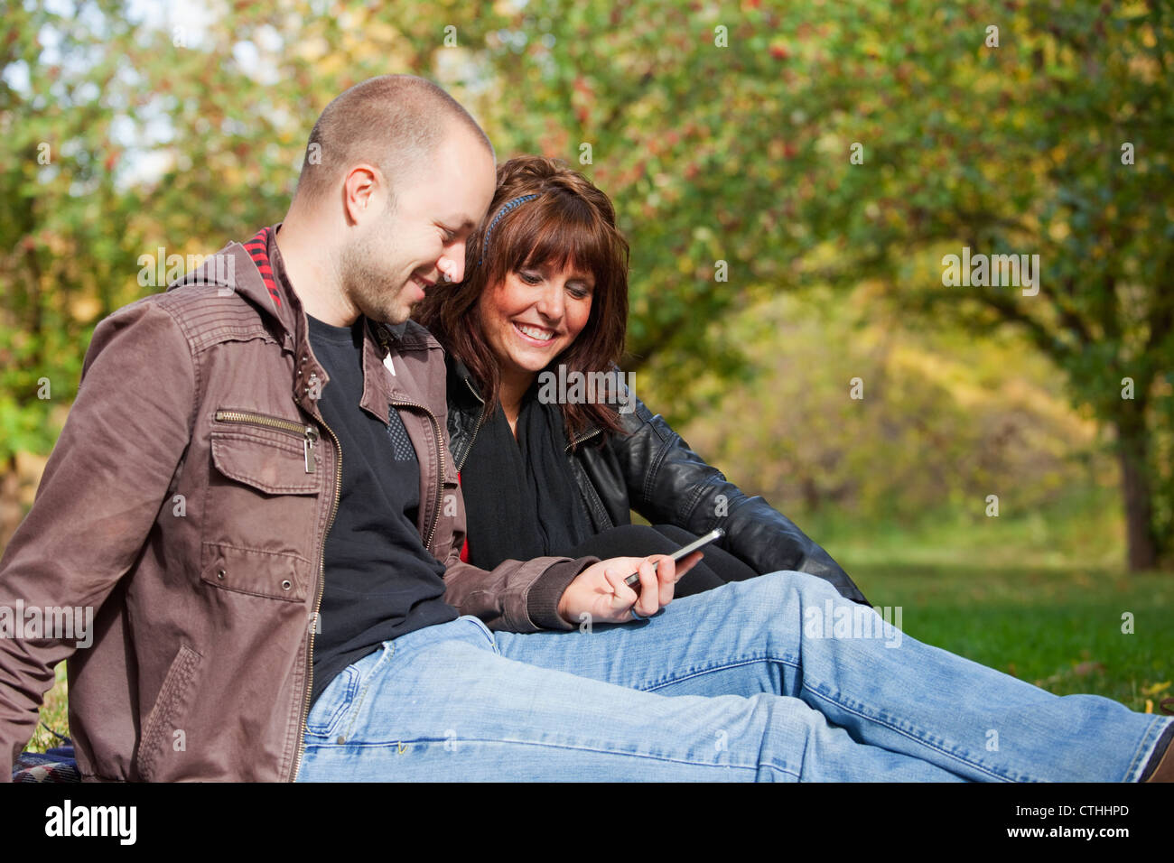 Giovane guardando i messaggi di testo nel parco; Edmonton, Alberta, Canada Foto Stock