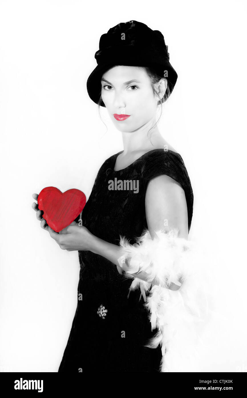 Una donna in un elegante abito nero tenendo un cuore rosso Foto Stock