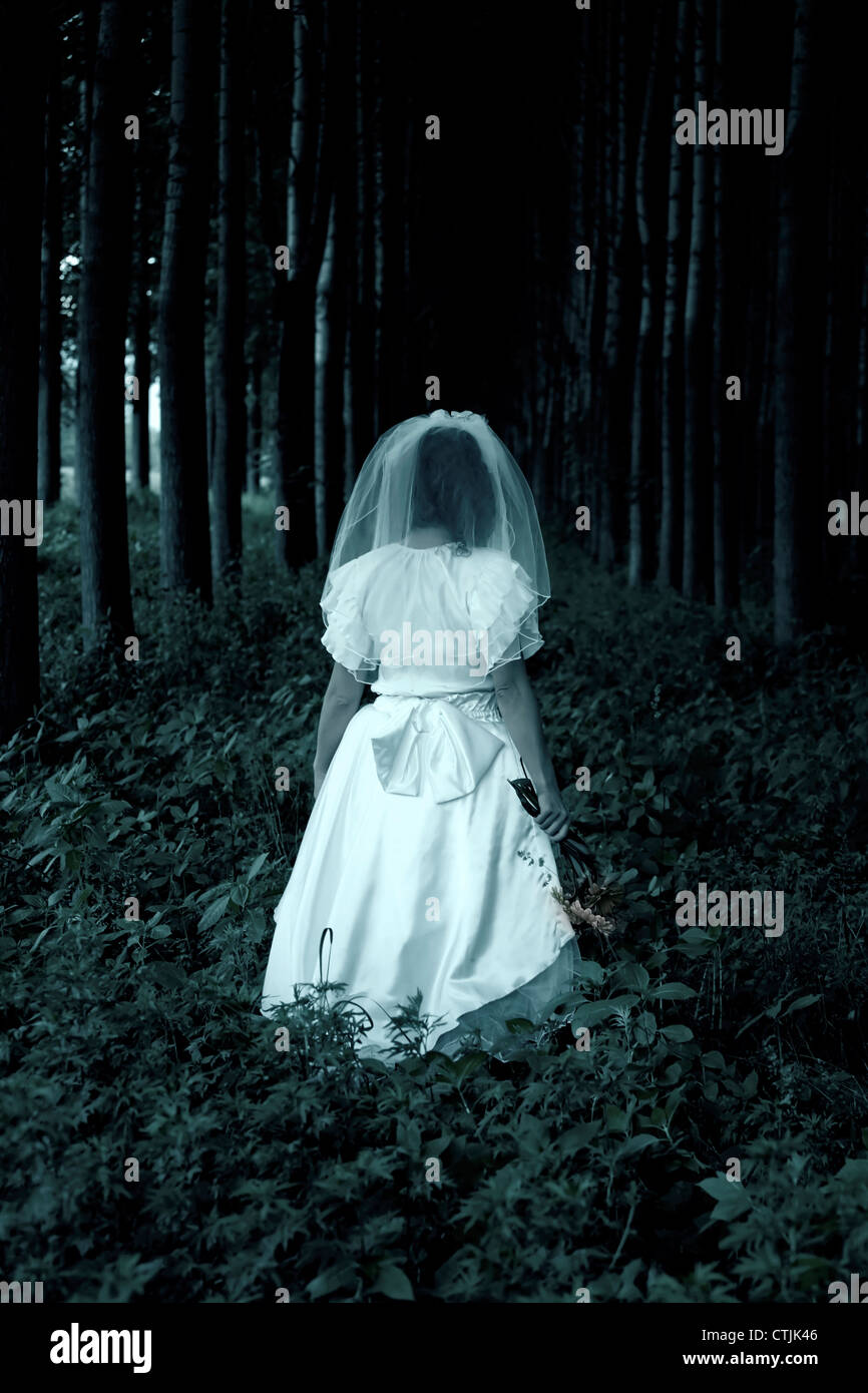 Una ragazza in un abito da sposa è a piedi attraverso una foresta Foto Stock