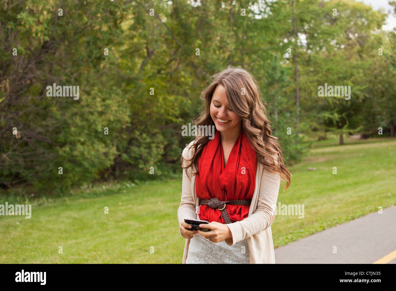 Giovane donna camminare in un parco e Texting; Edmonton, Alberta, Canada Foto Stock