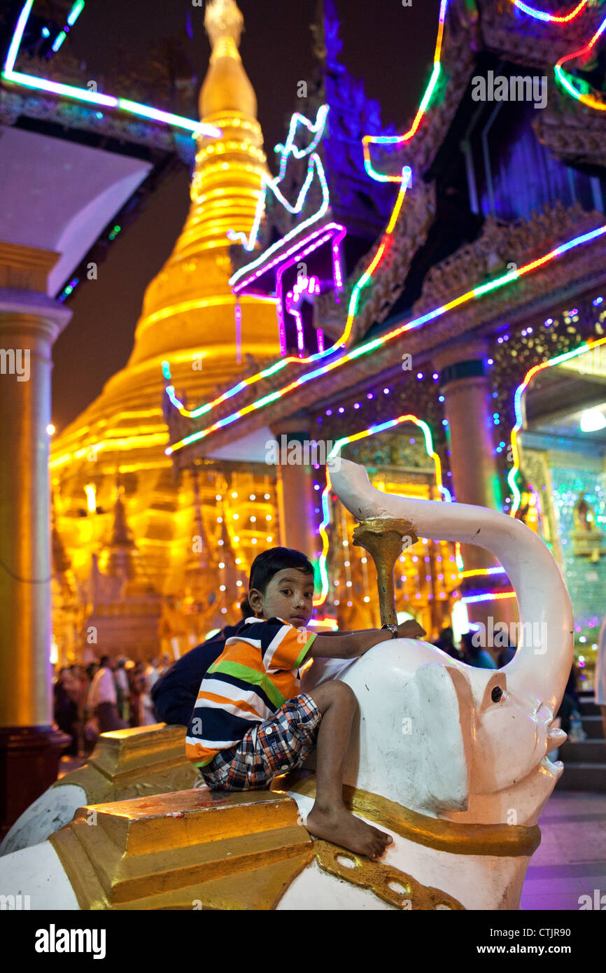 Un ragazzo si arrampica un elefante statua a motivi di illuminato di notte Shwedagon pagoda Yangon (Rangoon), Myanmar Foto Stock