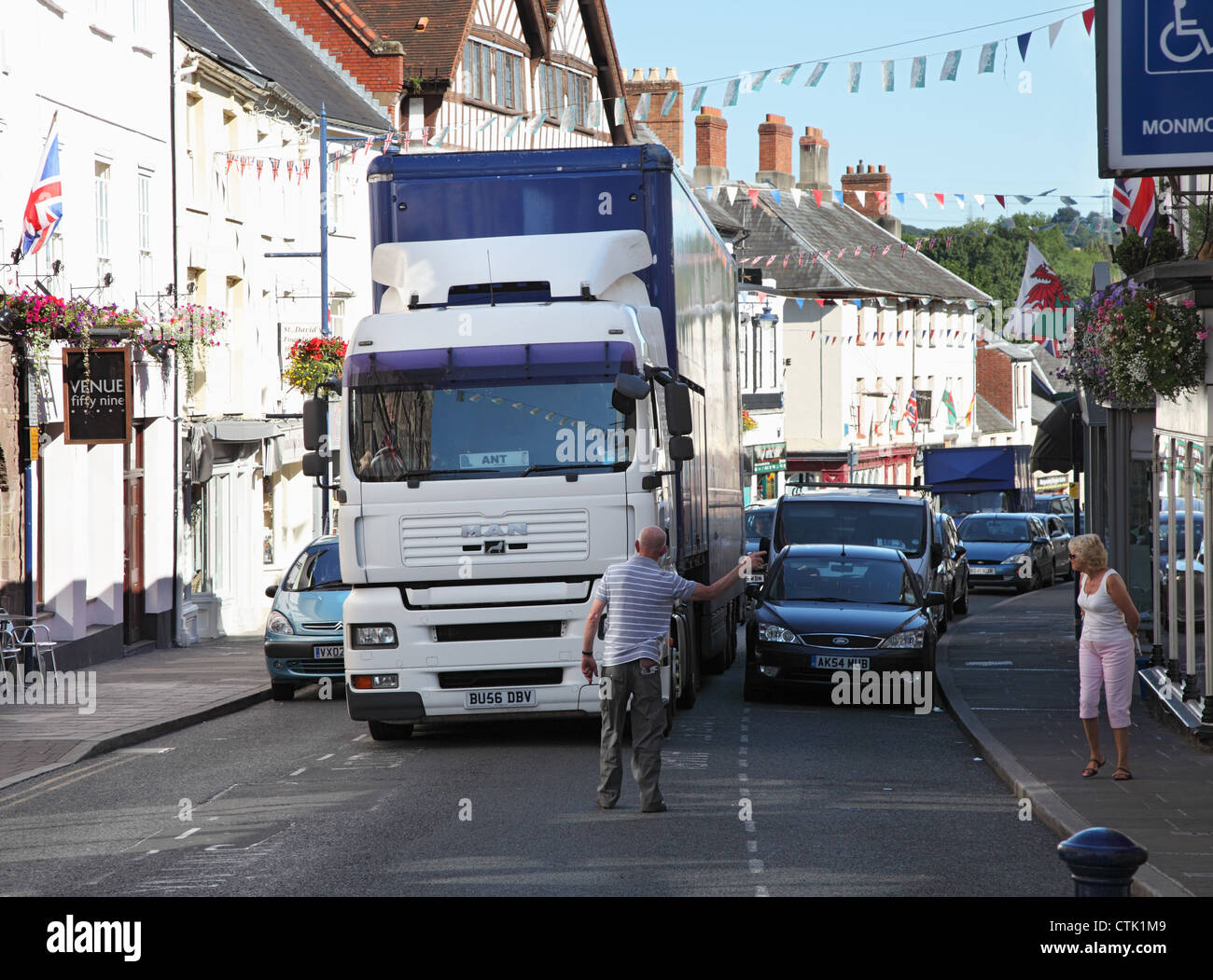 Un grande camion consegna le lotte per passare le macchine parcheggiate mentre un uomo aiuta a guidarlo attraverso. Cross Street, Abergavenny, Wales UK Foto Stock