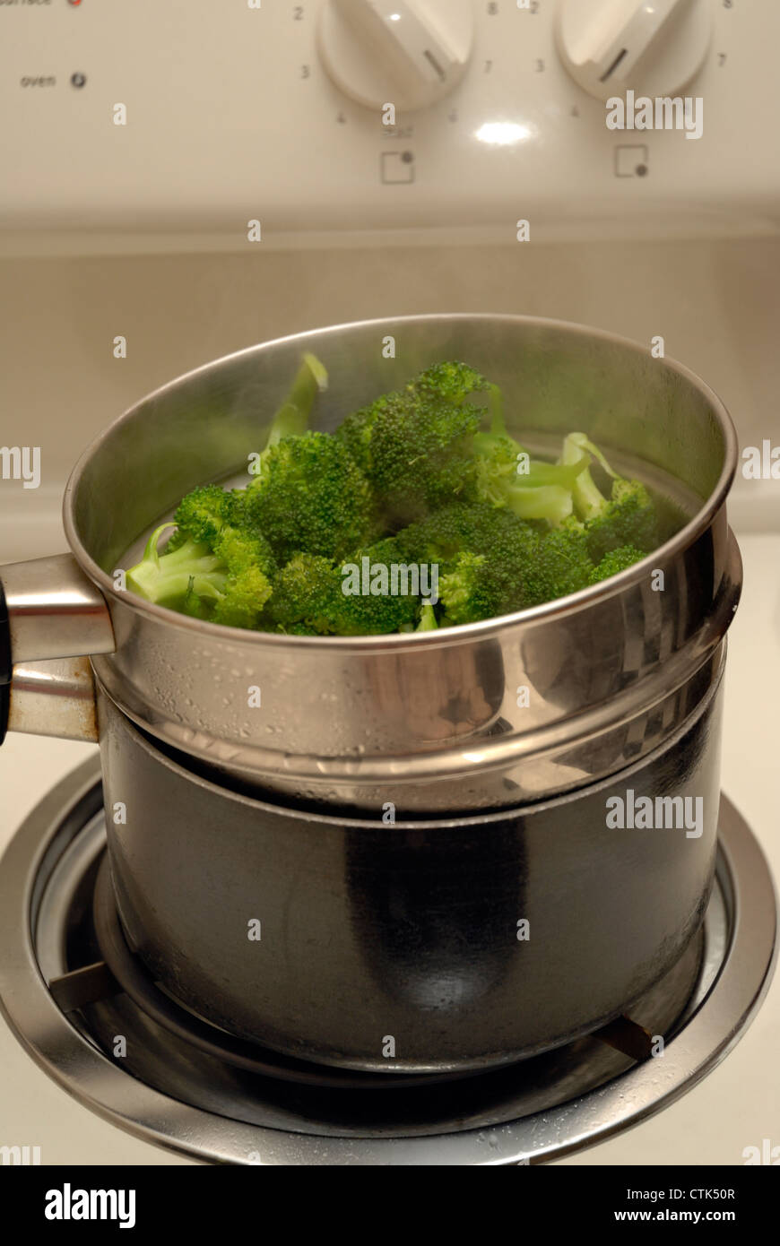 Broccoli la cottura a vapore in un tegame su un piano cottura. Il vapore è visibile salendo dalla parte superiore della teglia. Foto Stock