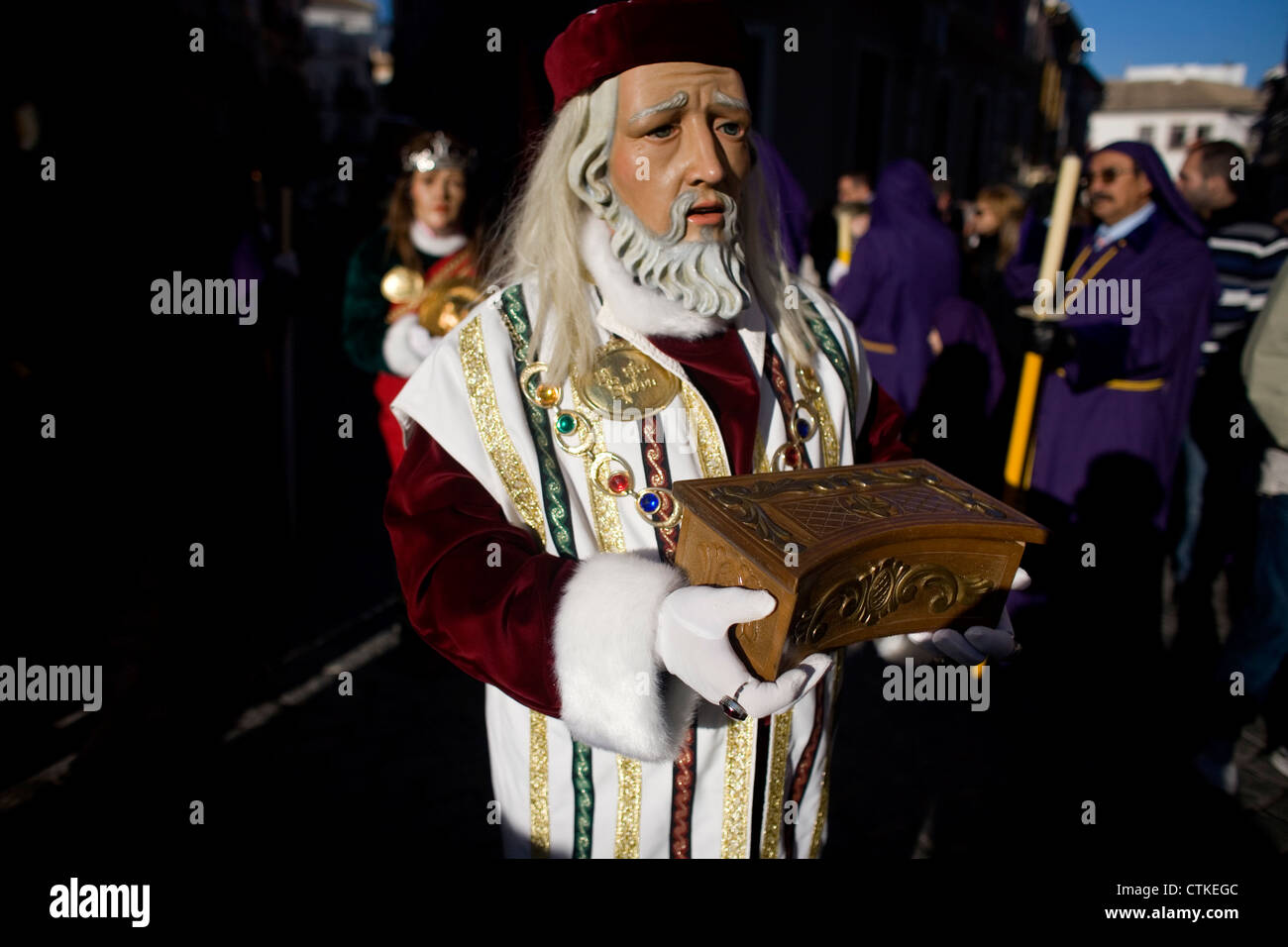 Un uomo mascherato vestito come un personaggio biblico contiene una scatola di legno durante una PASQUA SETTIMANA SANTA PROCESSIONE in Puente Genil, Spagna Foto Stock