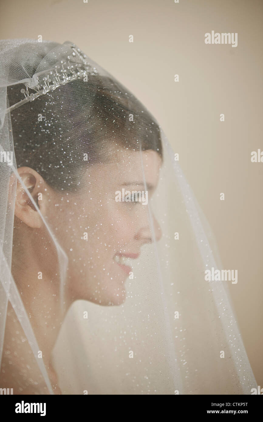Una giovane sposa che indossa un diadema e velo sorridente, vista laterale Foto Stock
