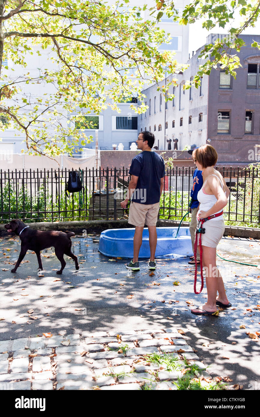 I proprietari di cani Labrador nero e plastica cane bagno di acqua su bella soleggiata giornata estiva a dog run in DeWitt Clinton park Manhattan Foto Stock