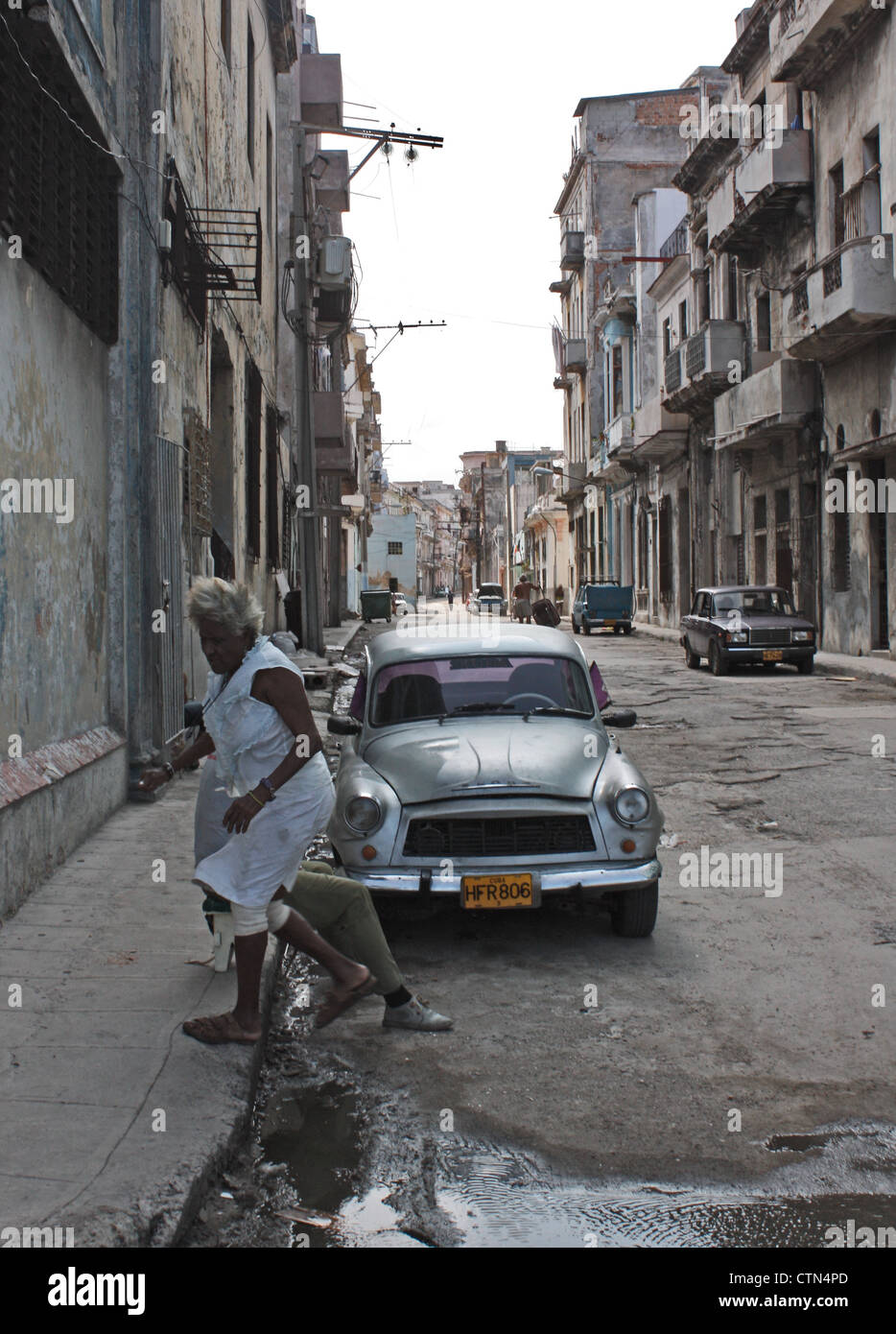 Una signora anziana passi fino sul marciapiede o pavimentazione evitando una pozza in una strada nel centro di Havana, Cuba Foto Stock