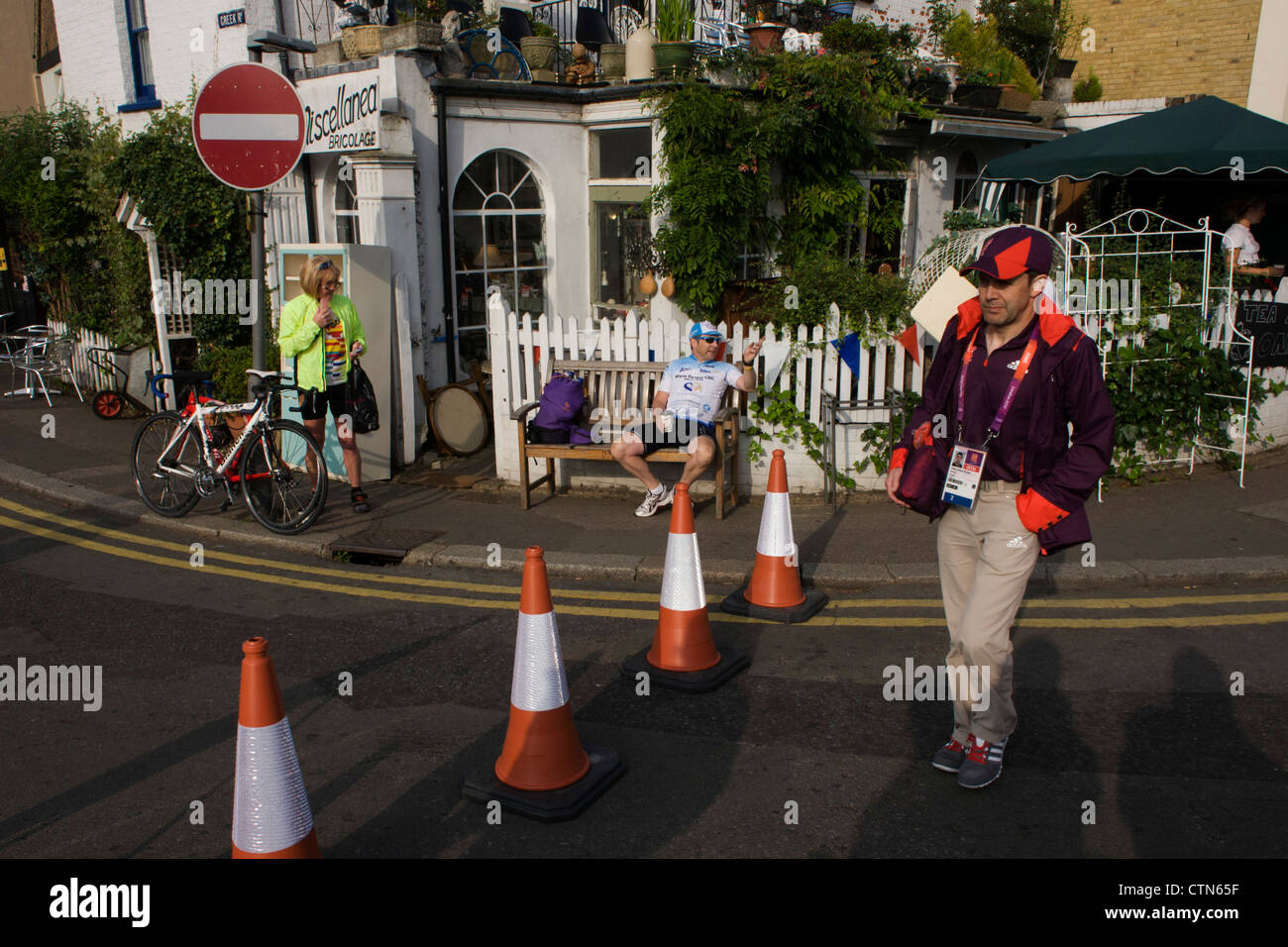 Giochi Olimpici Maker volontario attraversare una strada bloccata vicino a Hampton Court, a sud-ovest di Londra. Londra 2012 volontari sono chiamati 'Giochi Makers', come stanno contribuendo a rendere i giochi accadere. Fino a 70.000 giochi politici prendere su di una ampia varietà di ruoli attraverso le sedi: da accogliere i visitatori, per il trasporto di atleti; ad aiutare dietro le quinte nella tecnologia team per assicurarsi che i risultati visualizzare quanto più rapidamente e accuratamente possibile. Giochi politici provengono da una gamma diversificata di comunità e gli sfondi da tutto il Regno Unito e all'estero. Foto Stock