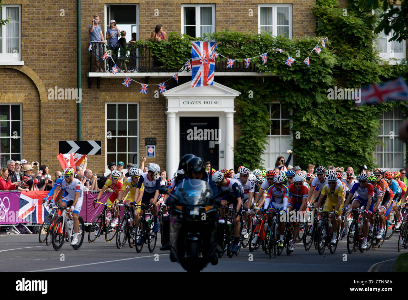 I ciclisti peloton velocità attraverso il Hampton Court a sud-ovest di Londra in concorrenza per il 250km mens' la gara su strada nella prima giornata di gara delle Olimpiadi di Londra 2012. A partire da Londra centrale e passando la capitale più famosi luoghi di interesse prima di uscire in Inghilterra rurale all'estenuante Box Hill nella contea del Surrey. Sud-ovest locali londinesi rivestito il percorso sperando per preferito britannico Mark Cavendish per vincere Team GB prima medaglia ma che sono poi stati delusi quando il Kazakistan è Alexandre Vinokourov alla fine ha vinto l'oro. Foto Stock