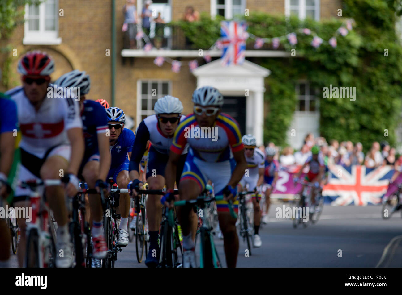 I ciclisti peloton velocità attraverso il Hampton Court a sud-ovest di Londra in concorrenza per il 250km mens' la gara su strada nella prima giornata di gara delle Olimpiadi di Londra 2012. A partire da Londra centrale e passando la capitale più famosi luoghi di interesse prima di uscire in Inghilterra rurale all'estenuante Box Hill nella contea del Surrey. Sud-ovest locali londinesi rivestito il percorso sperando per preferito britannico Mark Cavendish per vincere Team GB prima medaglia ma che sono poi stati delusi quando il Kazakistan è Alexandre Vinokourov alla fine ha vinto l'oro. Foto Stock