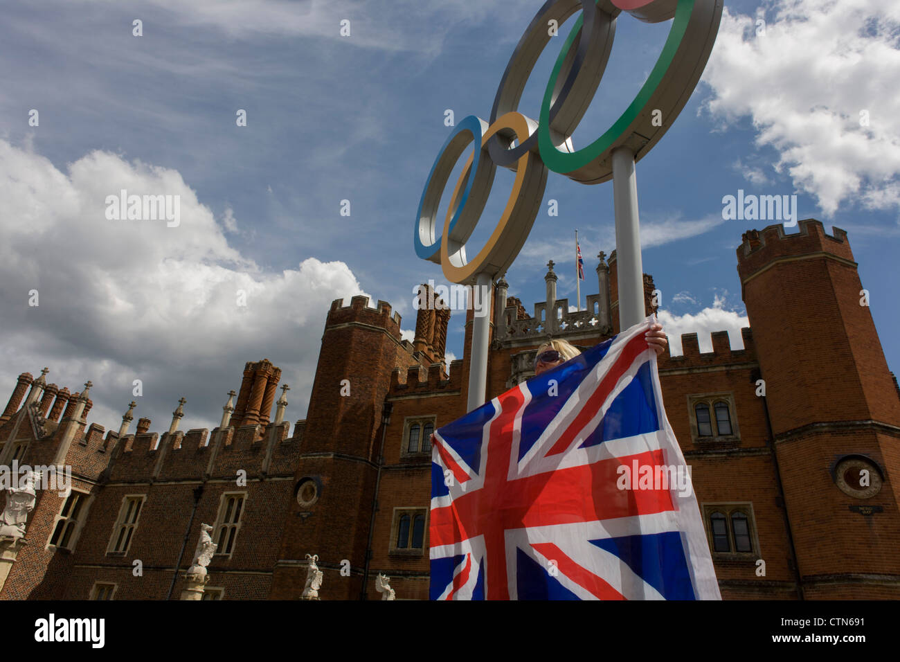 Londra lady si distingue per una foto souvenir sul anelli olimpici che stanno all'ingresso del Re Enrico VIII di Hampton Court Palace il primo giorno di gara del London 2012 Olympic 250km mens' la gara su strada. A partire da Londra centrale e passando la capitale più famosi luoghi di interesse prima di uscire in Inghilterra rurale all'estenuante Box Hill nella contea del Surrey. Sud-ovest locali londinesi rivestito il percorso sperando per preferito britannico Mark Cavendish per vincere Team GB prima medaglia ma che sono poi stati delusi quando il Kazakistan è Alexandre Vinokourov alla fine ha vinto l'oro. Foto Stock