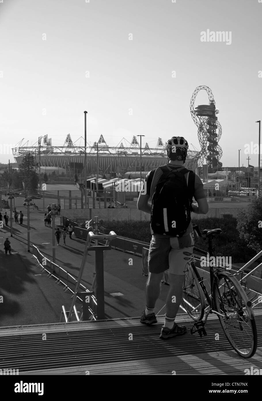 Ciclista sul ponte pedonale su Stratford High Street che mostra il 2012 Olympic Stadium e orbita in background. Foto Stock