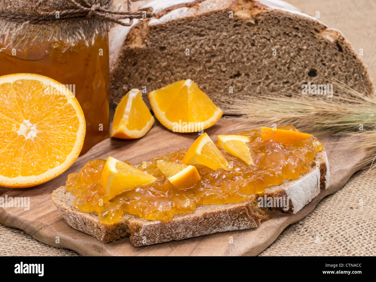 Pane con marmellata di arancio e frutta fresca su sfondo rustico Foto Stock