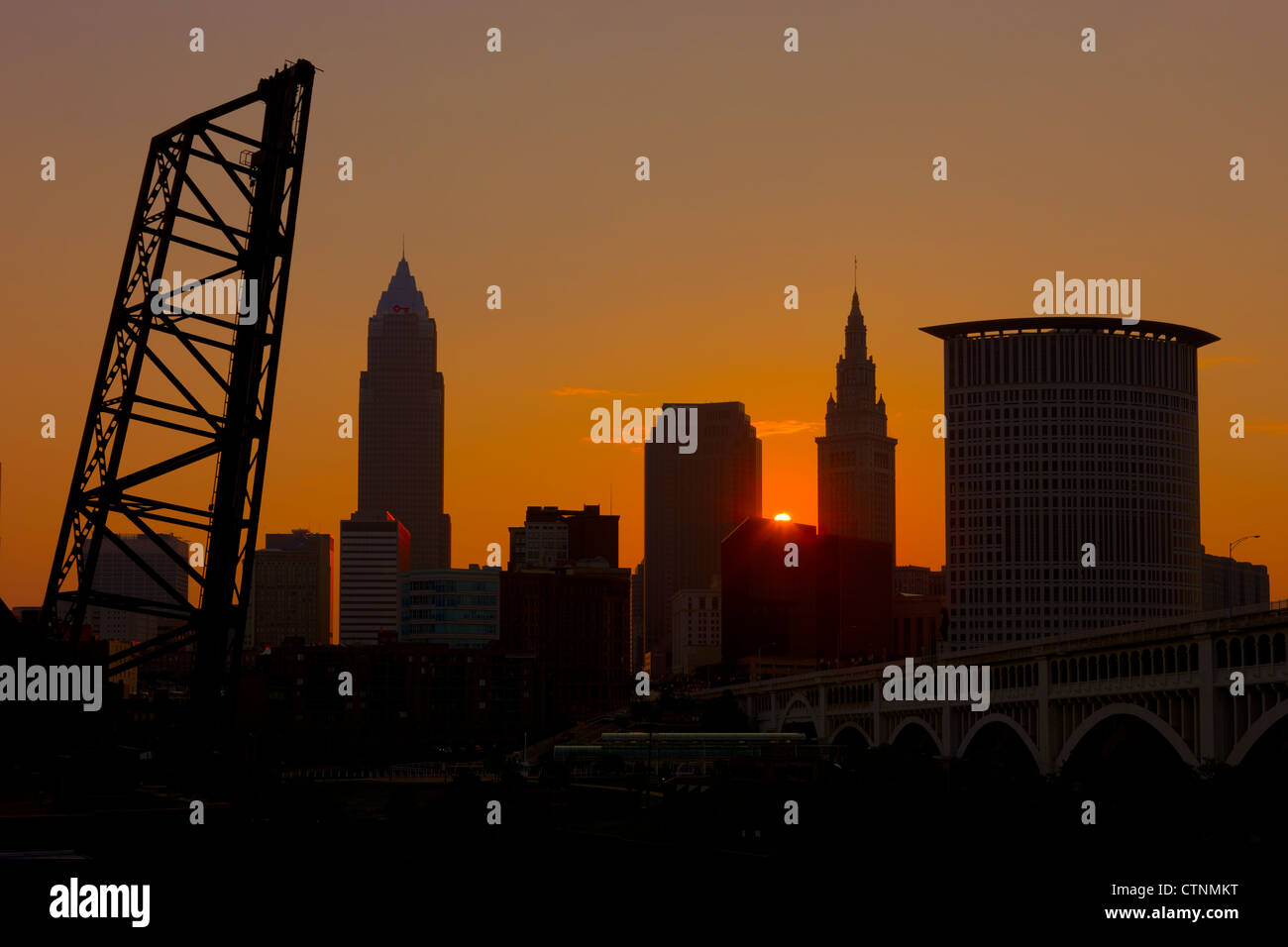 Il sole sorge su uno degli edifici del centro e proietta un bagliore arancione nel cielo dietro lo skyline di Cleveland, Ohio. Foto Stock