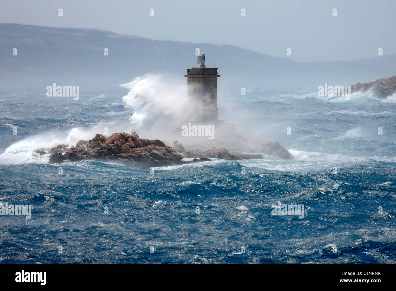 Le onde rompono oltre il faro. Foto Stock