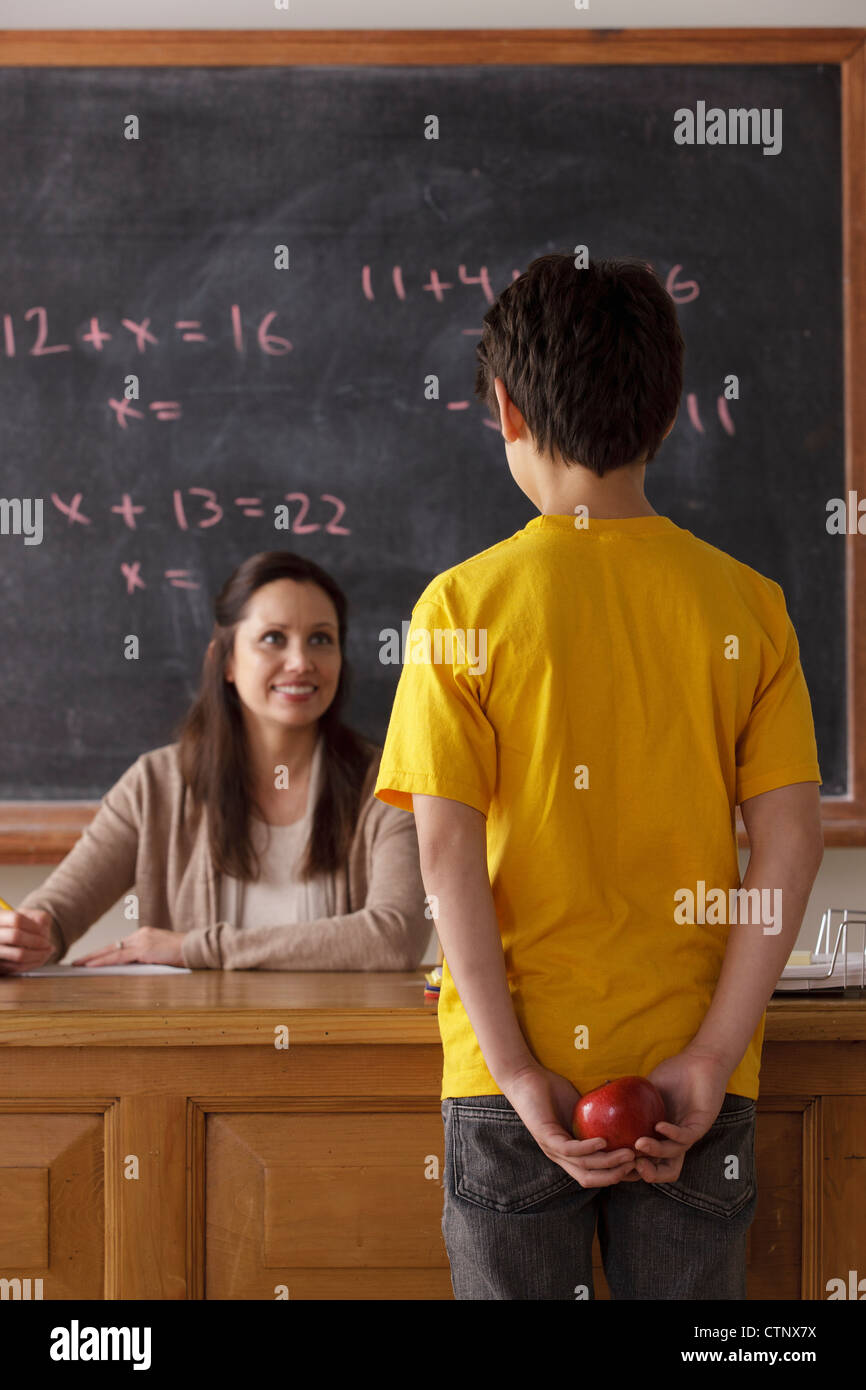 Stati Uniti, California, Los Angeles, schoolboy (12-13) azienda apple dietro la schiena con insegnante in background Foto Stock