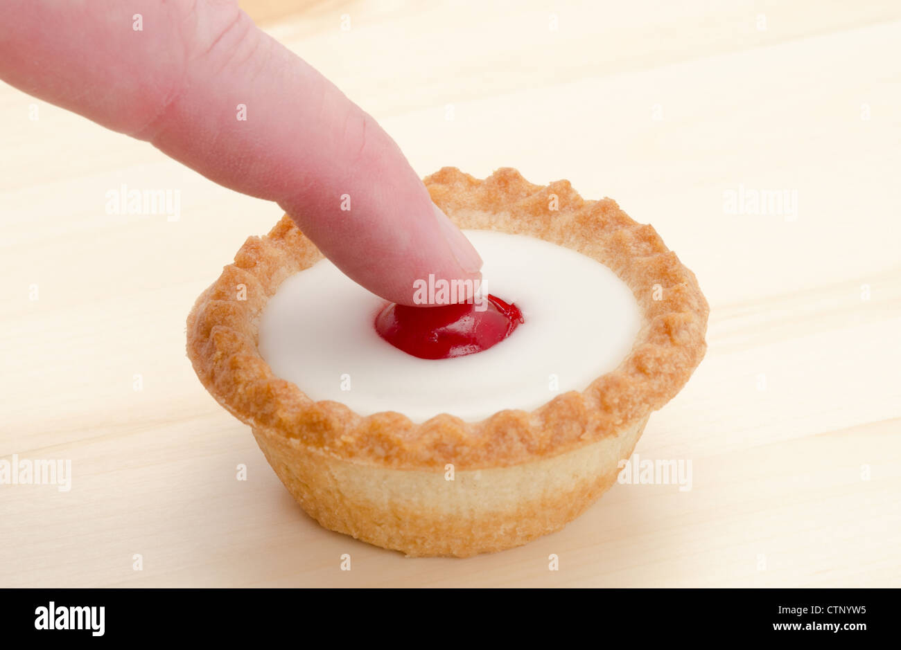 Premere il tasto ! Concetto di immagine di un dito di spinta sul la ciliegia nel centro di Bakewell tart torta. Foto Stock
