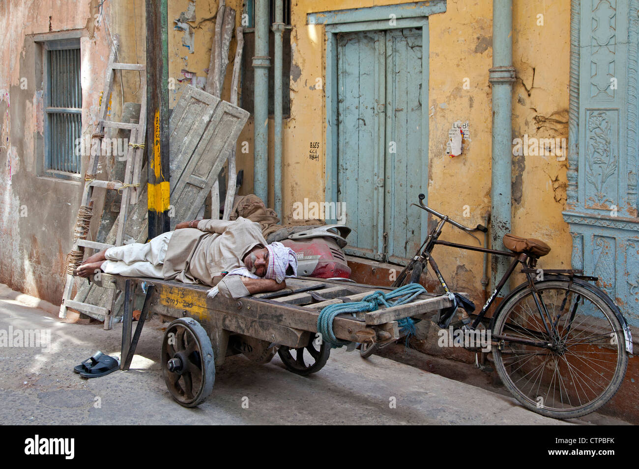 Il vecchio uomo dorme sul carrello di legno in strada nella Vecchia Delhi, India Foto Stock
