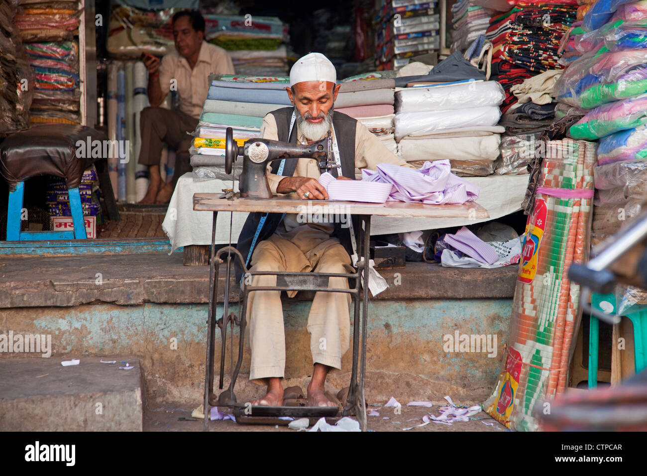 Sarto rendendo i vestiti su una vecchia macchina da cucire nella parte anteriore dello stabilimento di sartoria, Delhi, India Foto Stock