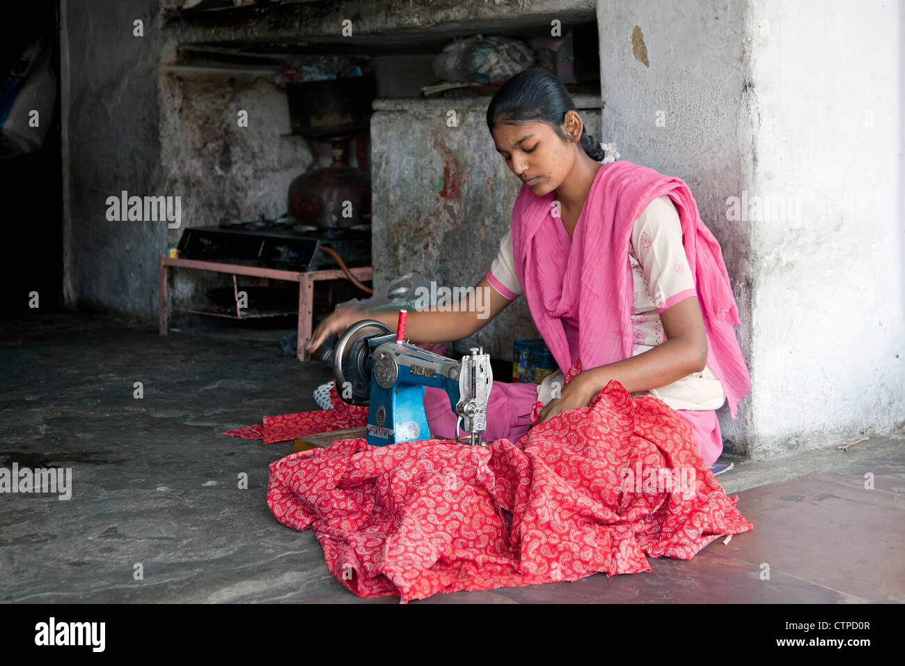 Indian ragazza seduta con le gambe incrociate a creare vestiti con la vecchia macchina da cucire al negozio di sartoria a Jaipur, Rajasthan, India Foto Stock