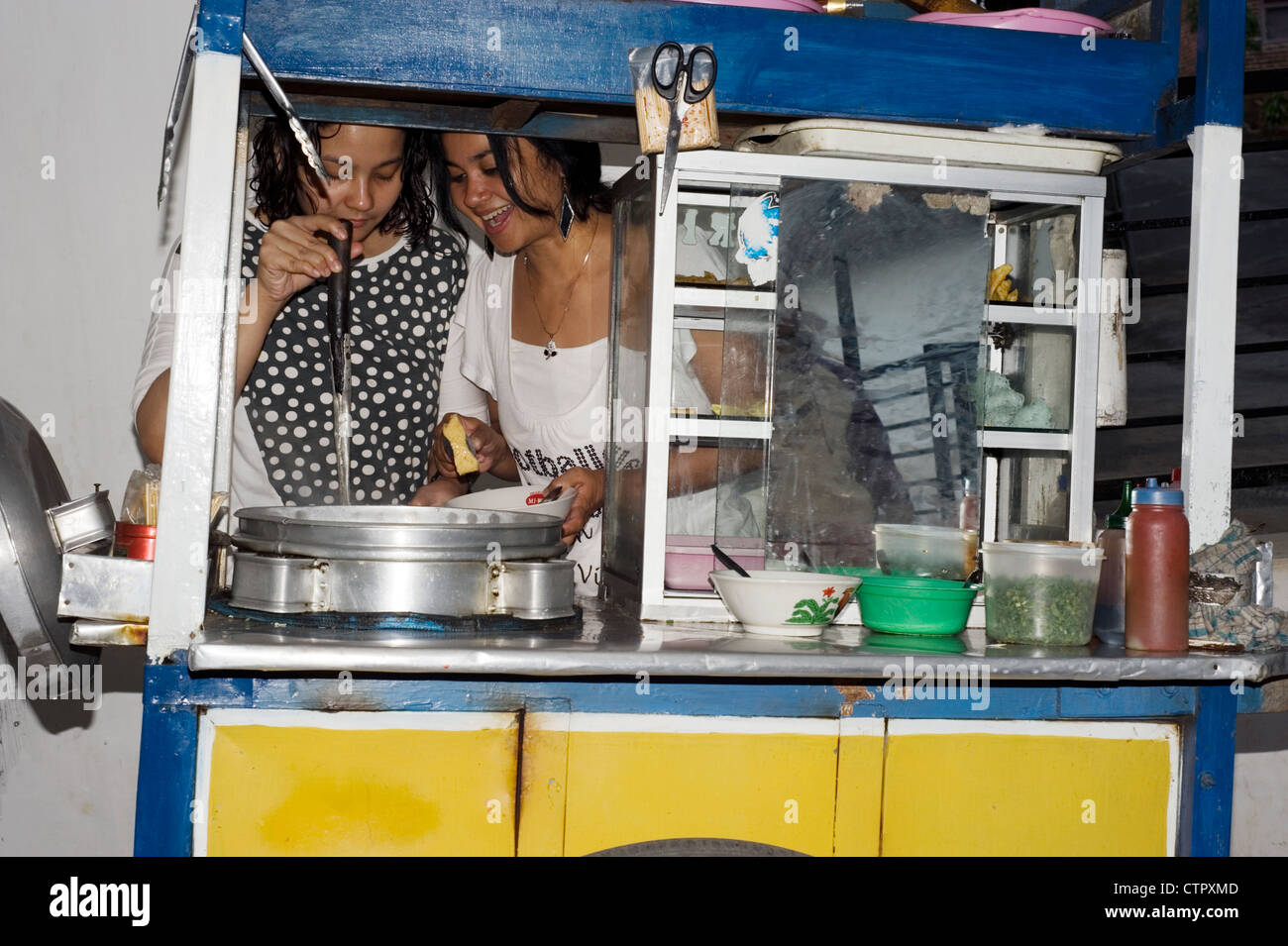 Due sorelle locale gustando un pasto di bakso da un carrello mobile in casa loro a malang java indonesia Foto Stock
