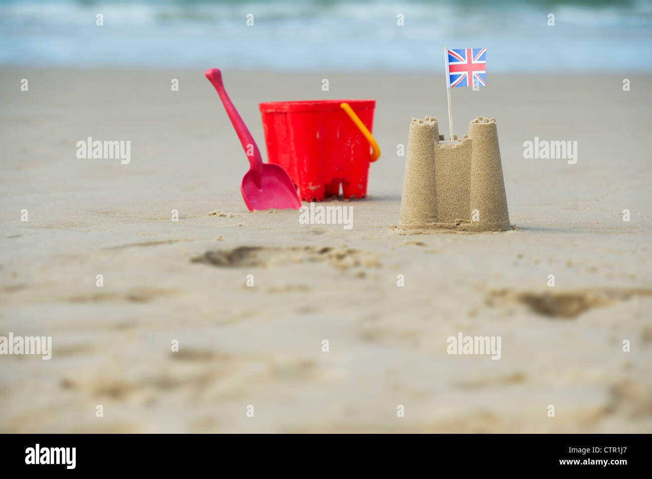 Union Jack flag in un castello di sabbia accanto a una benna childs e vanga su una spiaggia. Pozzetti accanto al mare. Norfolk, Inghilterra Foto Stock