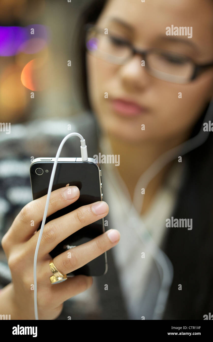 Giovane donna che indossa le cuffie ascoltando musica usando il suo iphone 4 Foto Stock