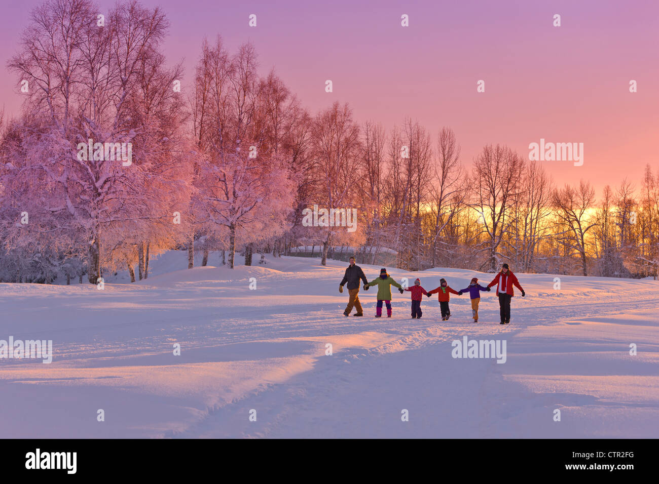 Gruppo familiare tenendo le mani a piedi sul percorso di neve tramonto bosco di betulle, in background Jack russo Springs Park centromeridionale di ancoraggio Foto Stock