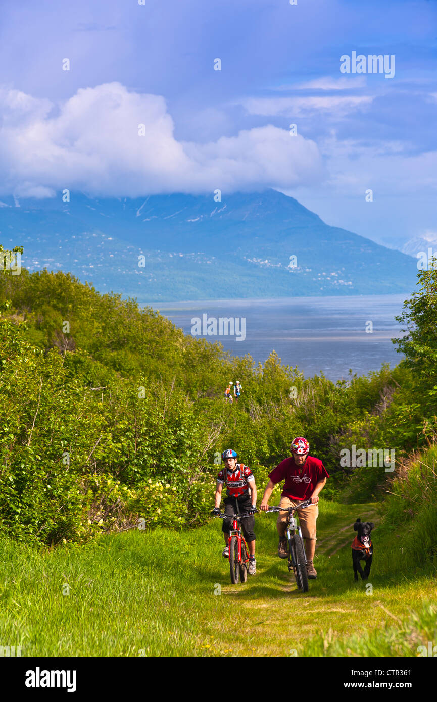 Due uomini mountain bike il loro cane sul sentiero nel Parco Kincaid vista Insenatura Cook in background centromeridionale Anchorage in Alaska estate Foto Stock