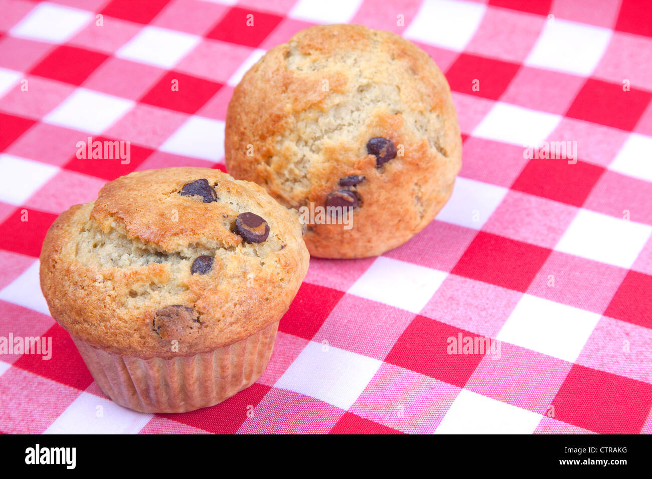 Una coppia di in casa banana chocolate chip muffin su un rosso Gingham tovaglia. Foto Stock