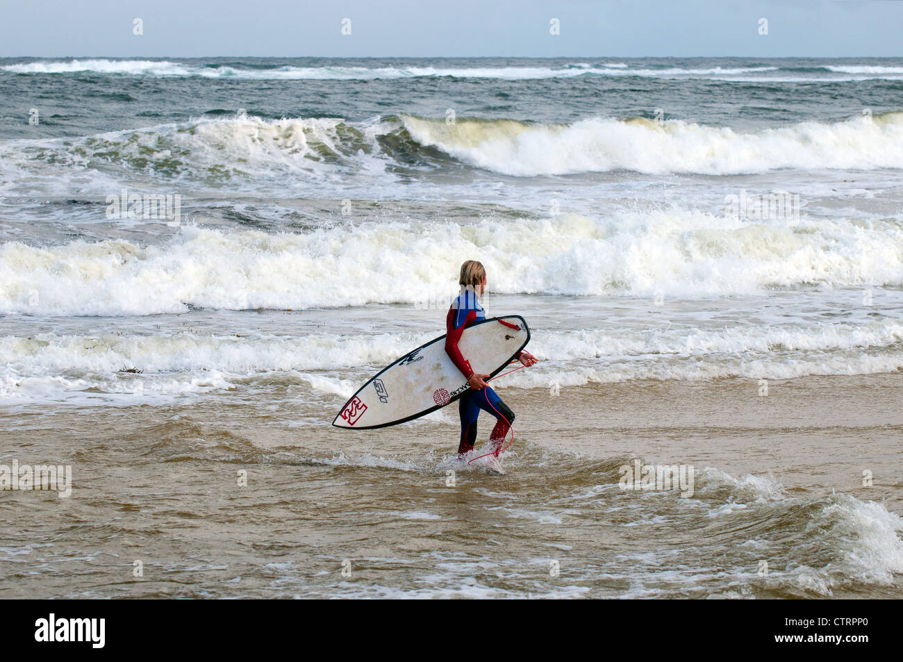 Un surfista a piedi al di fuori del mare al largo di Margaret River in Australia Occidentale. Foto Stock