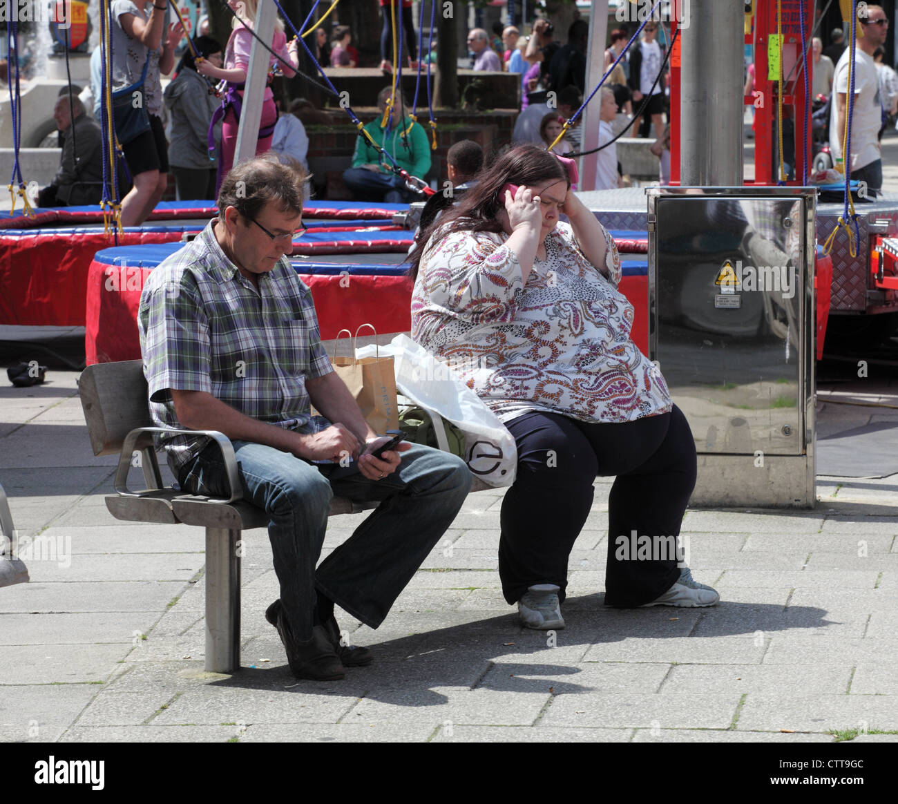 Uomo e donna obesa seduta sul banco di lavoro e utilizzando i telefoni cellulari di Portsmouth, England, Regno Unito Foto Stock