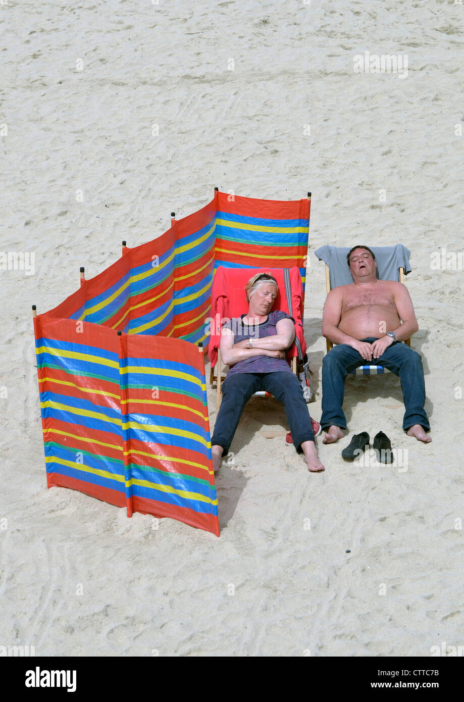L uomo e la donna di dormire sulla spiaggia sabbiosa di sedie a sdraio Foto Stock