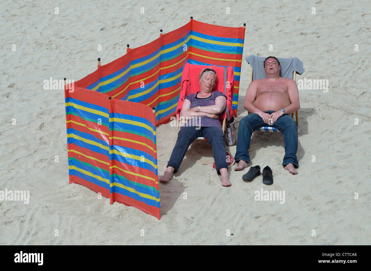 Uomo di mezza età e donne addormentato sulla spiaggia sabbiosa Foto Stock