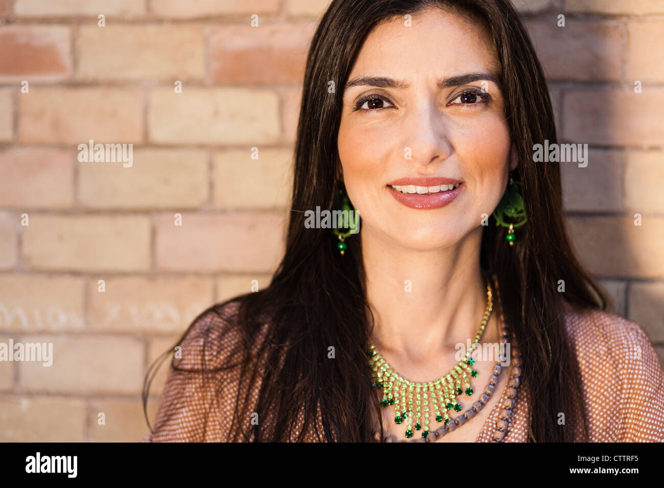 Close-up di una donna sorridente con un sfondo mattone (trucco e gioielli) Foto Stock